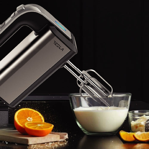 Tesla hand mixer on a kitchen counter with oranges and a bowl of milk.
